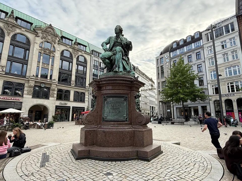 Lessing-Denkmal mit Inschriftentafel auf rundem Podest, umgeben von historischen Geschäftshäusern am Gänsemarkt