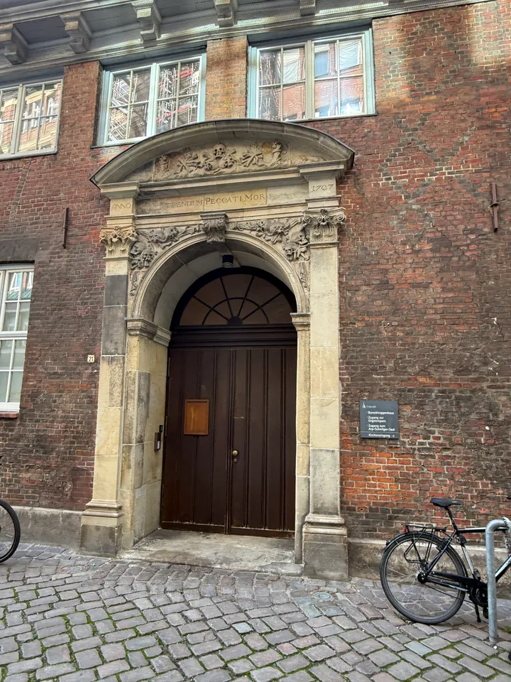 Barockes Sandsteinportal mit Totenschädelrelief, Inschrift von 1707 und dunkler Holztür in einer Backsteinwand