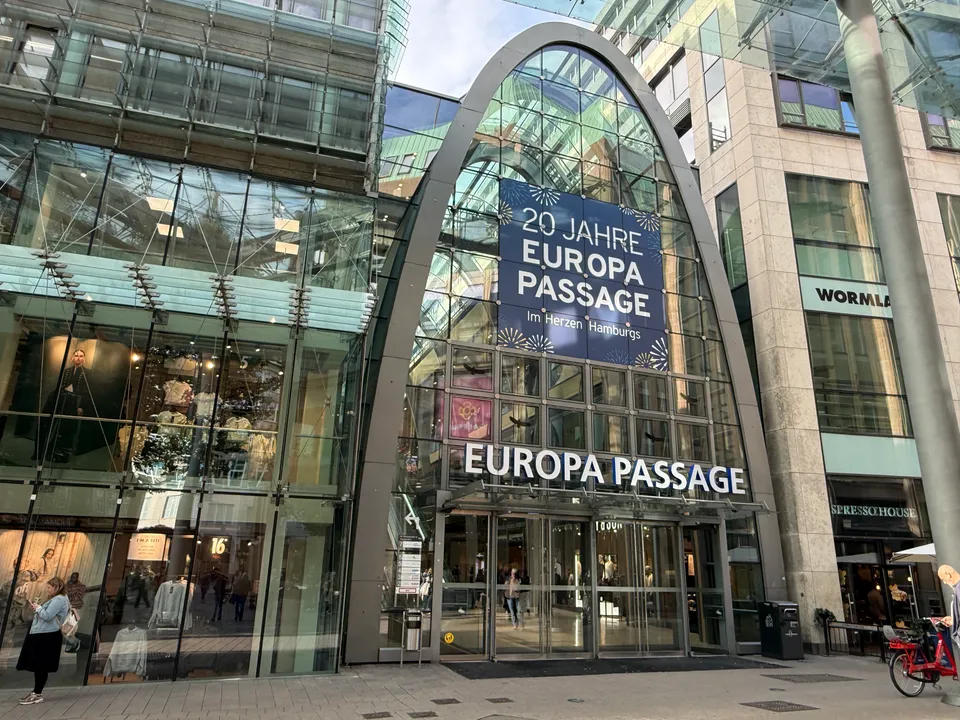 Glasbogen am Haupteingang der Europa Passage Hamburg mit Jubiläumsbanner, Schriftzug über dem Eingang und angrenzenden Geschäftsfassaden