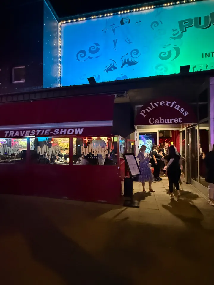 Eingang des Pulverfass Cabaret mit roter Markise, Wintergarten mit Aufschrift Travestie-Show und wartenden Gästen, nachts