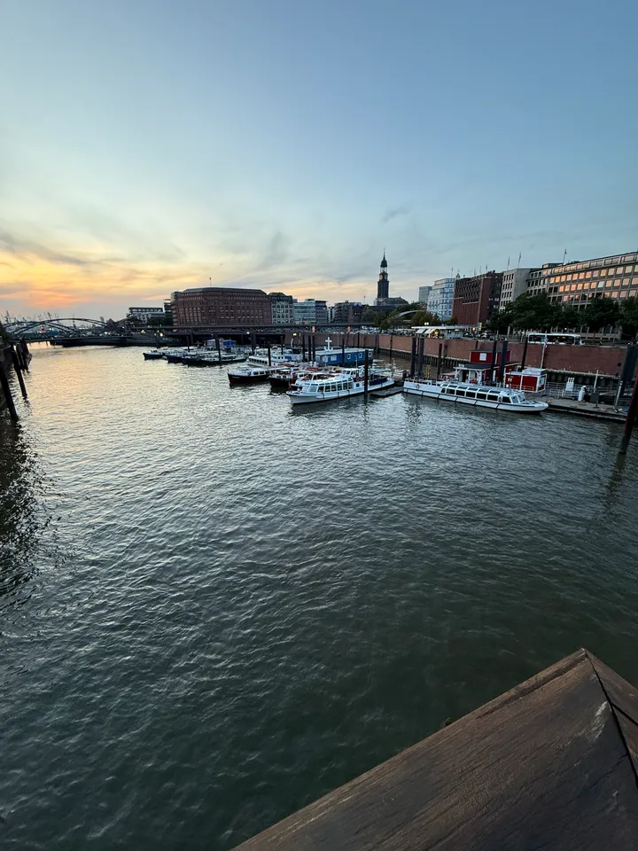 Hafenbecken in der Abenddämmerung mit angelegten Fahrgastschiffen, Backsteingebäuden und dem Turm des Michel im Hintergrund