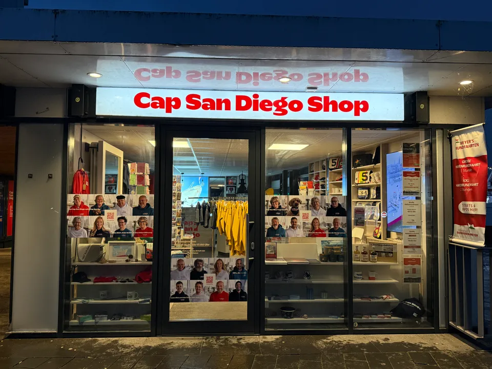 Beleuchtete Ladenfront des Cap San Diego Shops mit Schaufenstern voller Fanartikel und Plakaten an den Scheiben