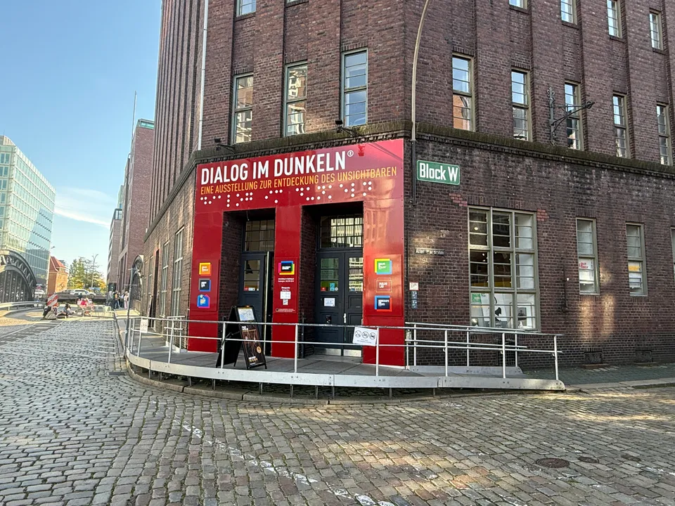 Roter Eingang der Ausstellung Dialog im Dunkeln an einem Backstein-Speicherbau mit Rampe und Kopfsteinpflaster