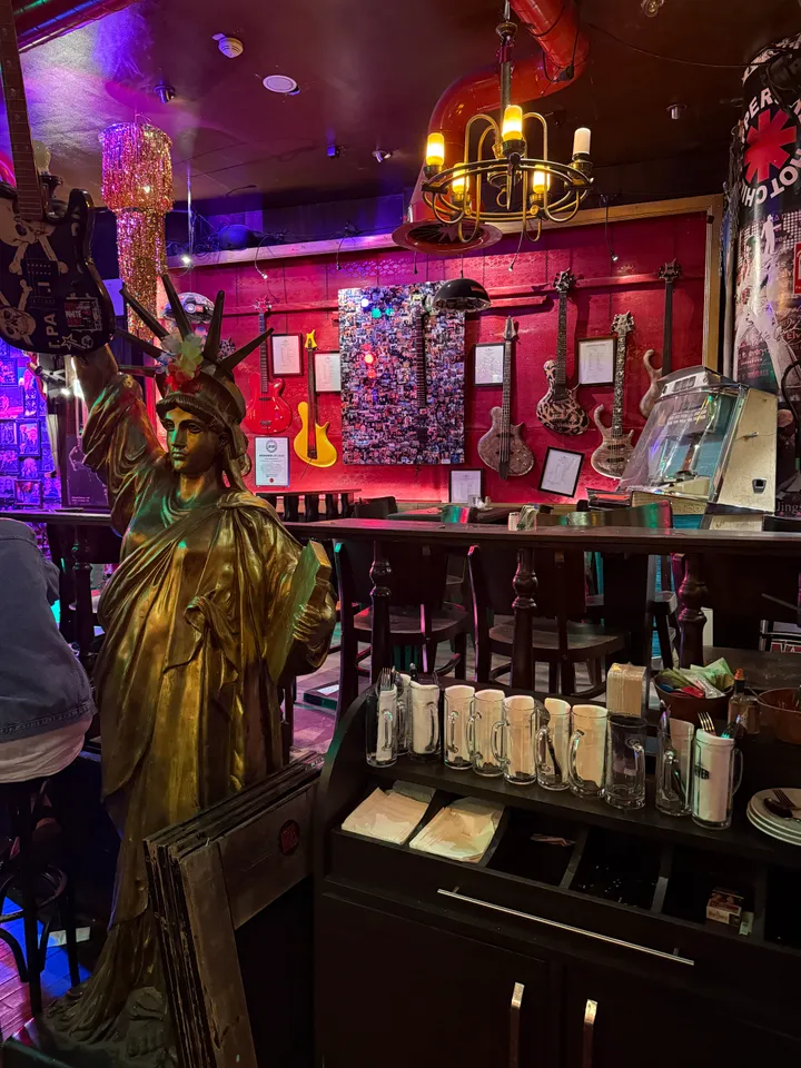 Goldene Freiheitsstatue-Figur vor einer roten Wand mit Gitarren, Kerzenleuchter, Jukebox und Serviertisch mit Bierkrügen