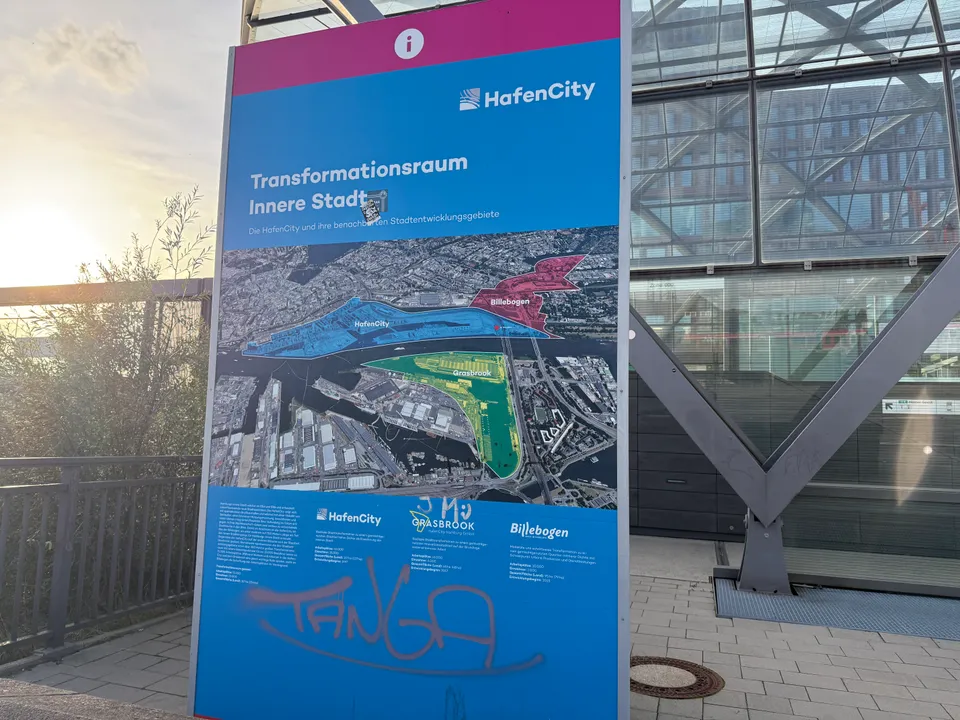 HafenCity-Infotafel „Transformationsraum Innere Stadt“ mit Luftbildkarte von HafenCity, Grasbrook und Billebogen vor einer Glasfassade