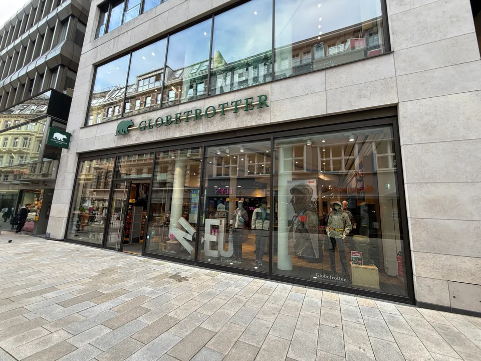 Ladenfassade von Globetrotter mit grünem Schriftzug, Schaufenstern mit Outdoor-Bekleidung und heller Steinfassade an gepflasterter Fußgängerzone