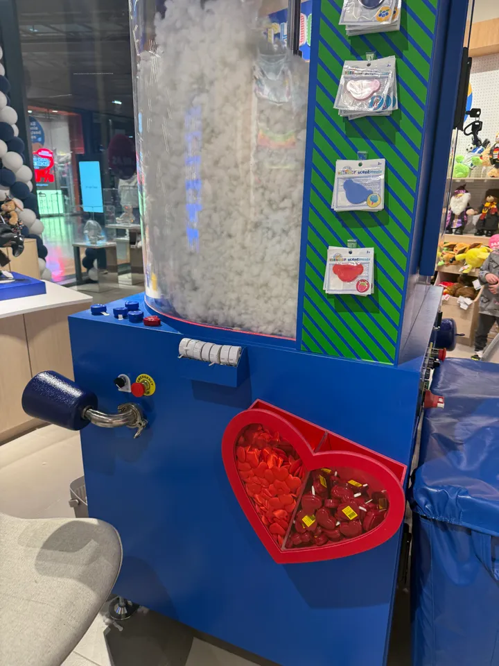 Blaue Füllmaschine mit Füllrohr, Wattebehälter und herzförmiger Schale voller roter Stoff- und Kunststoffherzen
