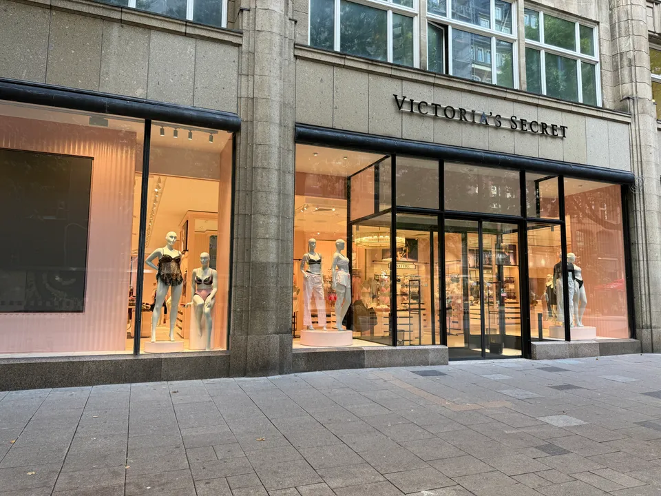 Ladenfront von Victoria's Secret mit Natursteinfassade, beleuchteten Schaufenstern, Schaufensterpuppen in Dessous und gepflastertem Gehweg davor