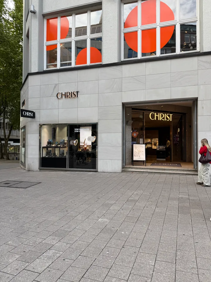 Eingang und Schaufenster des Juweliergeschäfts CHRIST an einem hellen Eckgebäude in einer gepflasterten Fußgängerzone