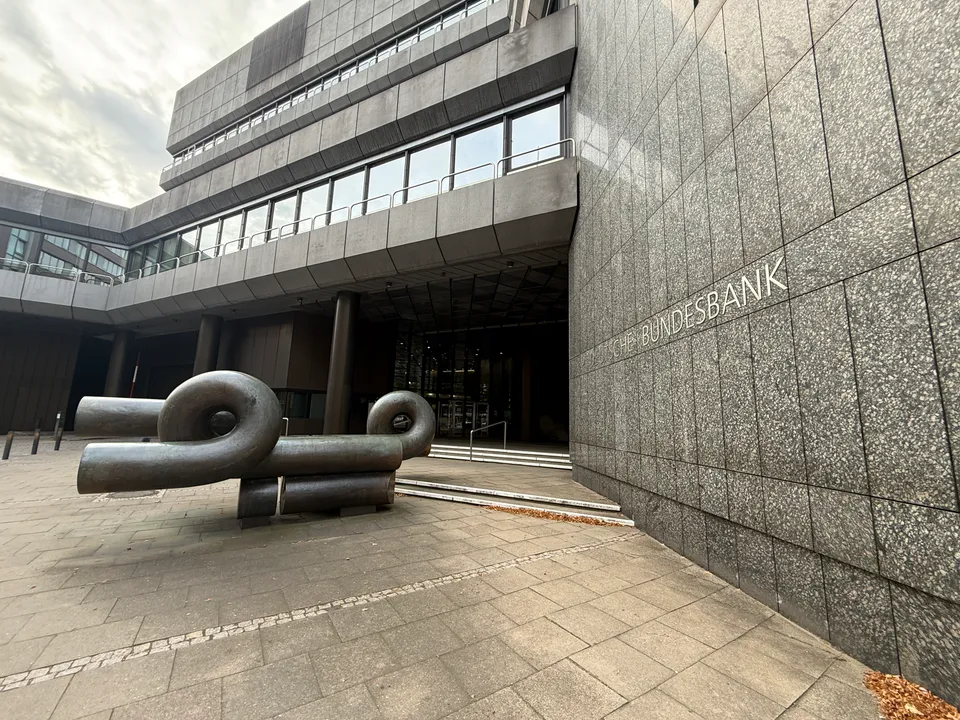 Bronzeskulptur aus gebogenen Rohren vor verglastem Eingang, rechts Granitwand mit Schriftzug Bundesbank