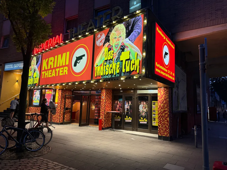 Beleuchteter Eingang des Imperial Theaters mit großen Krimi-Plakaten, Seitenschild und Glastüren am Abend