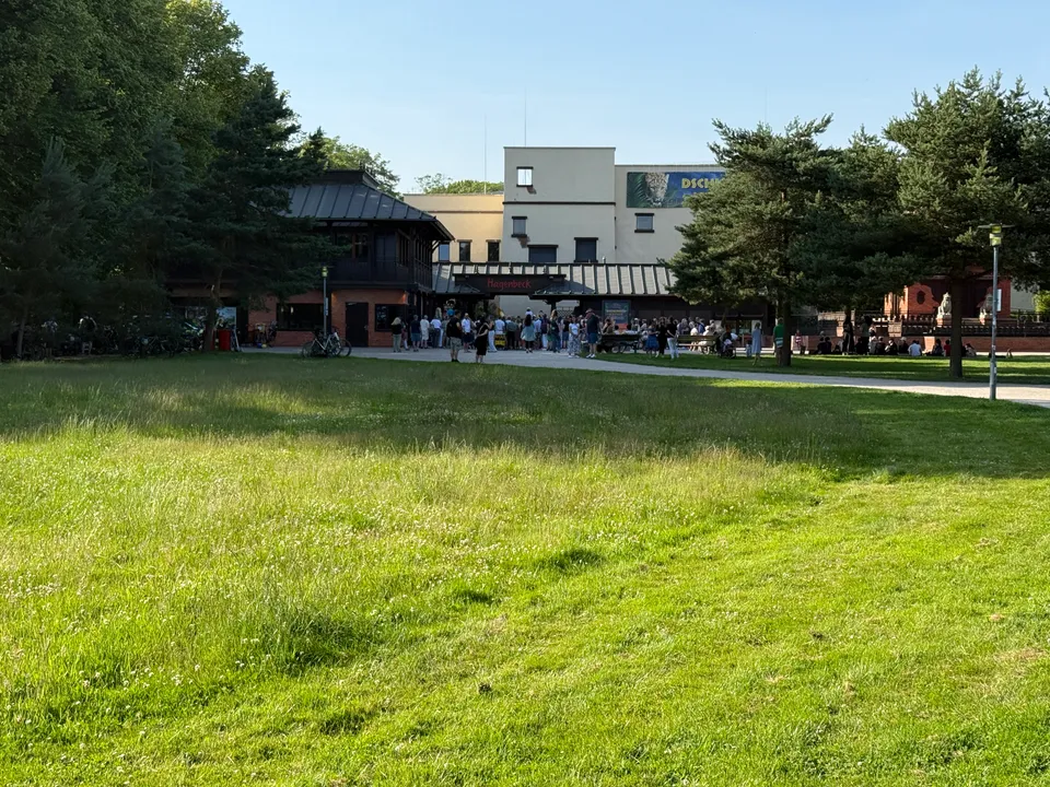 Rasenfläche vor dem Eingang des Tierparks Hagenbeck mit wartenden Besuchern und hellem Gebäude dahinter