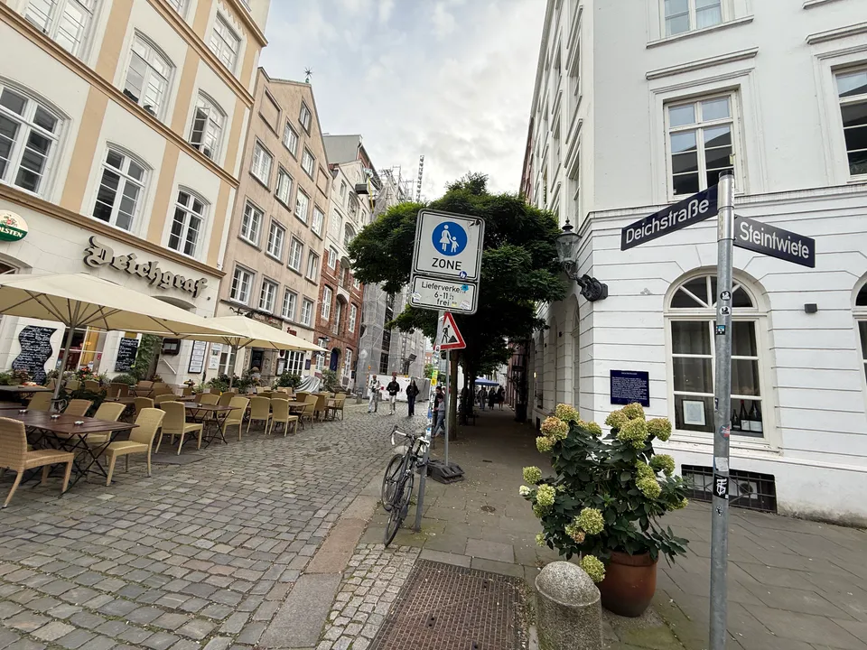 Gepflasterte Deichstraße mit historischen Häusern, Außenbestuhlung des Restaurants Deichgraf, Fußgängerzonenschild und Straßenschild Deichstraße/Steintwiete