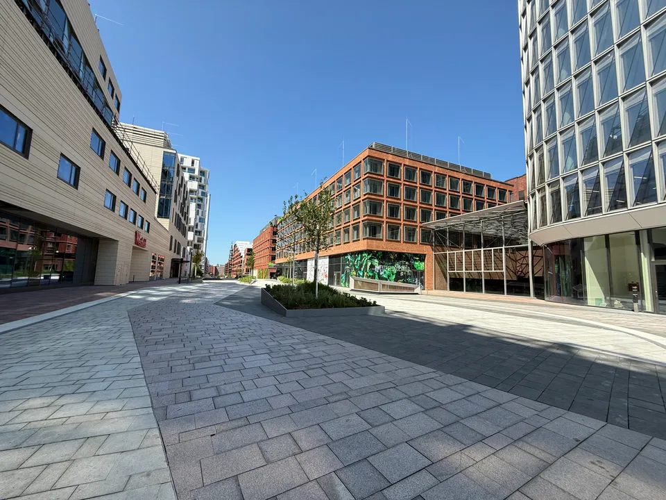 Leere gepflasterte Fußgängerzone zwischen hellem Westfield-Gebäude, rotem Ziegelbau mit grünem Wandbild und rundem Glasturm