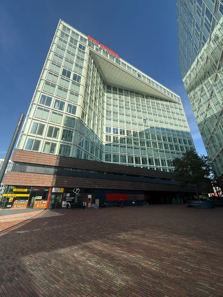 Gläsernes SPIEGEL-Hochhaus mit Fassadeneinschnitt und Läden im Klinkersockel hinter einem gepflasterten Platz