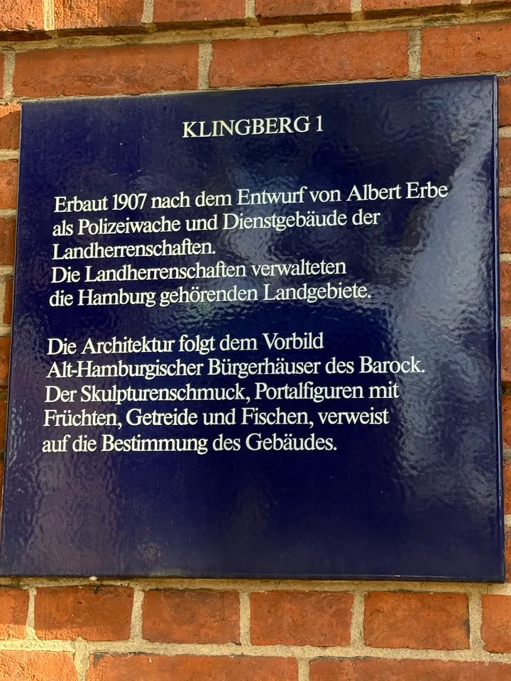 Dunkelblaue Informationstafel mit weißer Schrift zur Geschichte des Gebäudes Klingberg 1 an einer Backsteinwand