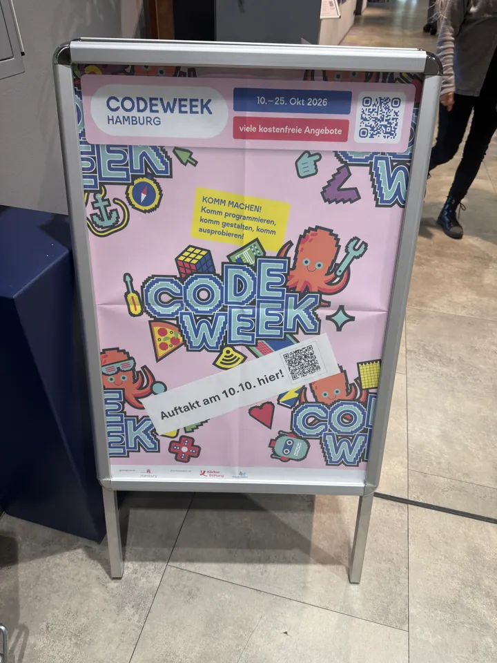 Kundenstopper mit rosafarbenem Plakat der Codeweek Hamburg, 10. bis 25. Oktober 2026, auf Fliesenboden