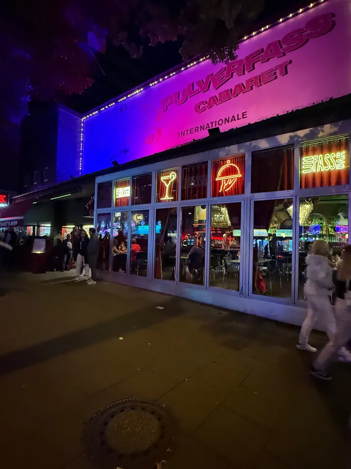 Violett beleuchtetes Transparent Pulverfass Cabaret über verglaster Front mit Neonzeichen, nachts, Passanten auf dem Gehweg