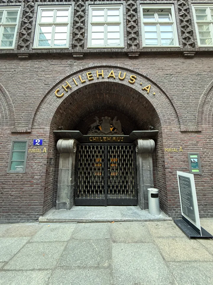 Rundbogenportal A des Chilehauses mit goldenem Schriftzug, Wappenrelief und schmiedeeisernem Gittertor