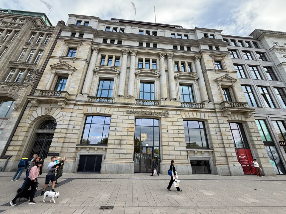 Historische Sandsteinfassade der Commerzbank mit Säulen und großen Glasfenstern, davor Passanten auf dem gepflasterten Gehweg