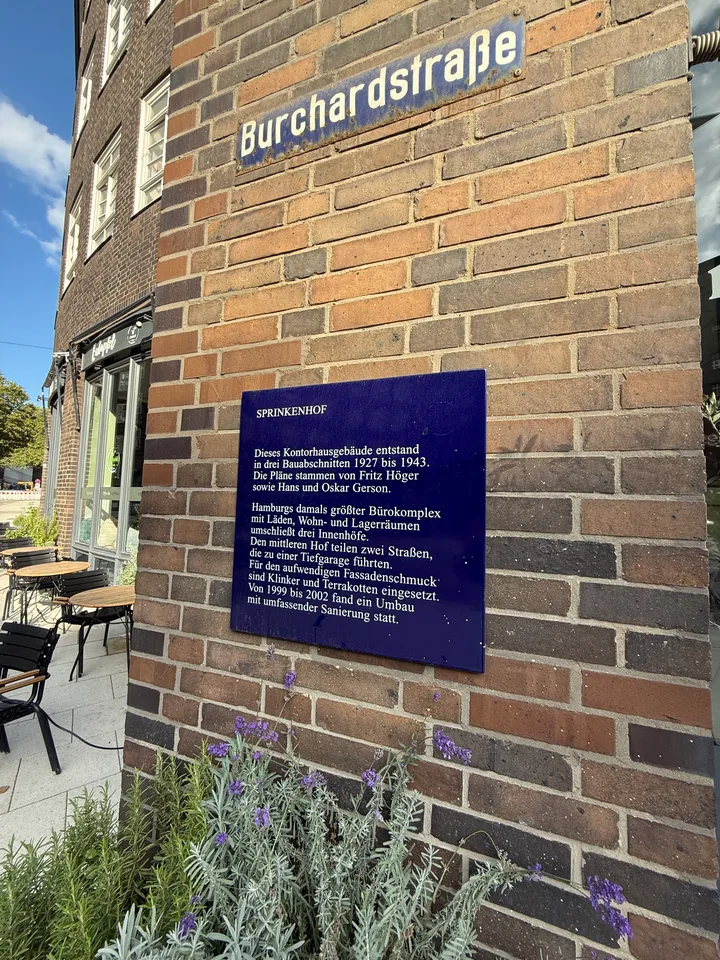 Straßenschild Burchardstraße und blaue Informationstafel zum Sprinkenhof an einer Klinkerwand, davor blühender Lavendel