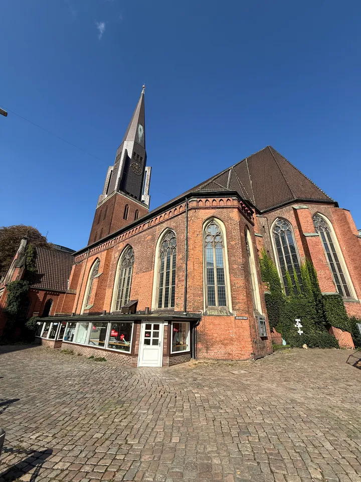 Gotische Backsteinkirche mit spitzem Turm und hohen Fenstern hinter einem weiten Platz mit Kopfsteinpflaster