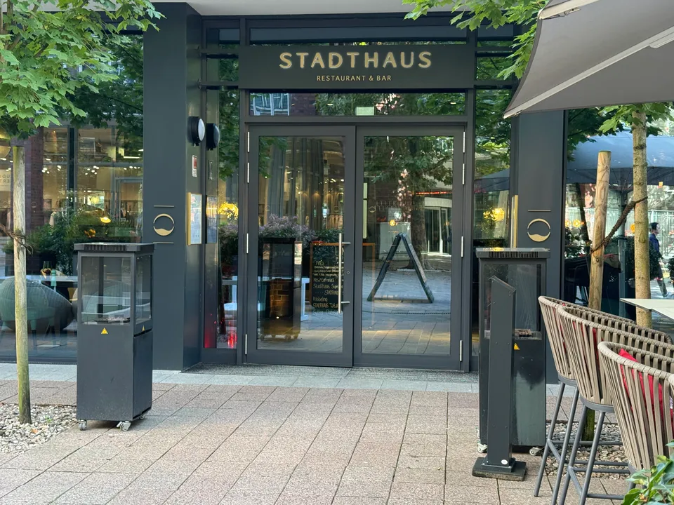 Glastür eines Restaurants unter dunklem Schild mit goldener Aufschrift Stadthaus Restaurant & Bar, daneben Heizstrahler