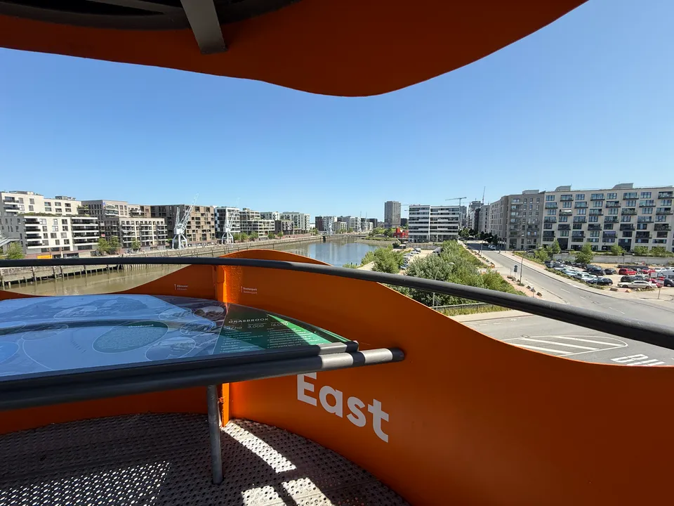 Infotisch auf orangefarbener Aussichtsplattform mit Blick nach Osten über Hafenbecken und Wohnneubauten