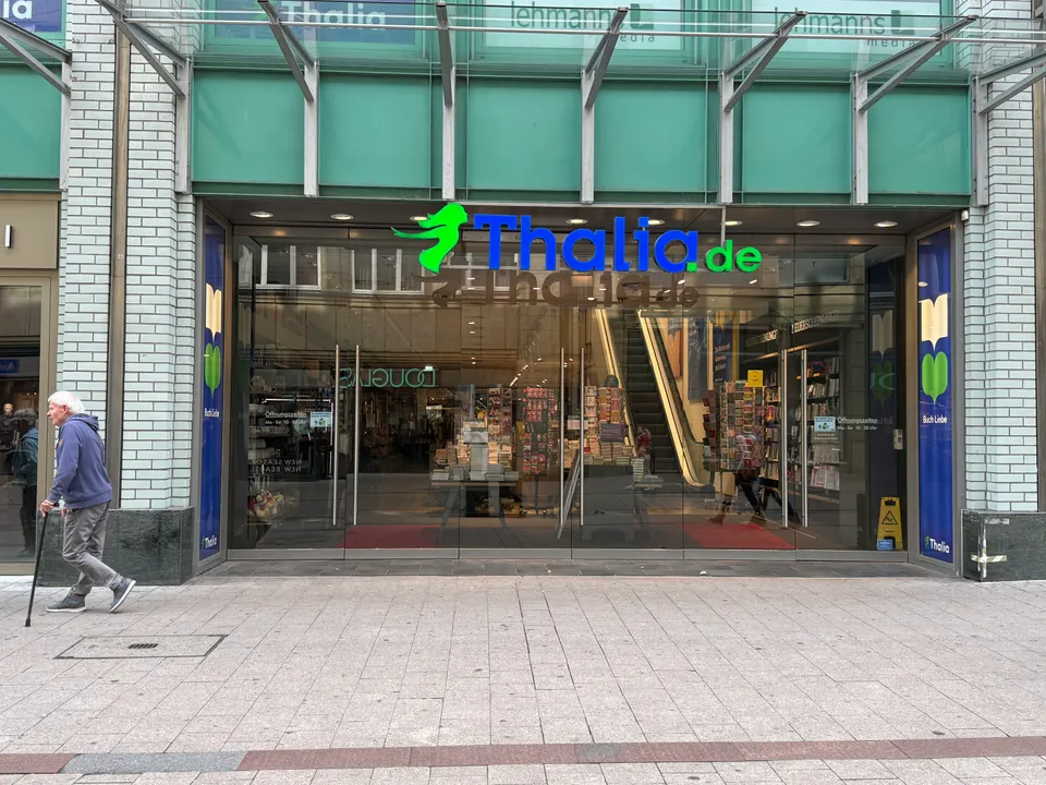 Verglaster Eingang der Thalia-Buchhandlung mit grün-blauem Schriftzug, davor Fußgängerzone mit Steinpflaster und ein Passant