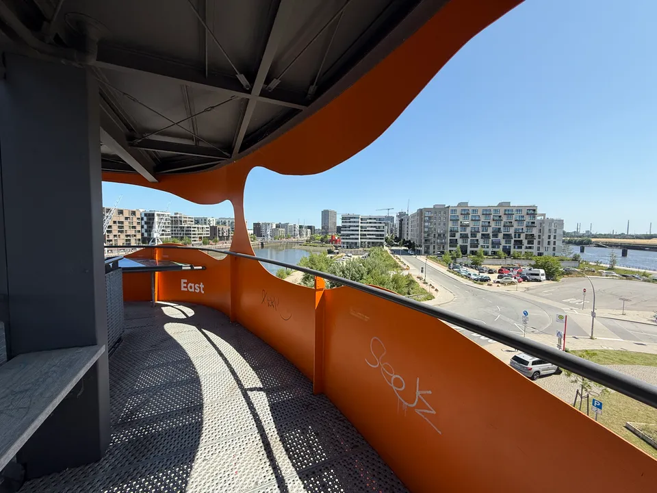 Umlaufender Gang der orangefarbenen Aussichtsplattform mit Blick auf Hafenbecken, Neubauten und Kräne