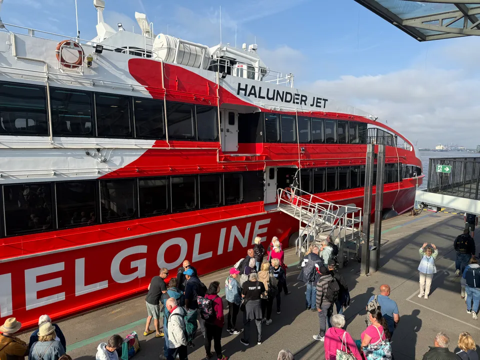 Fahrgäste warten vor der Einstiegstreppe des rot-weißen Katamarans „Halunder Jet“ mit Schriftzug Helgoline