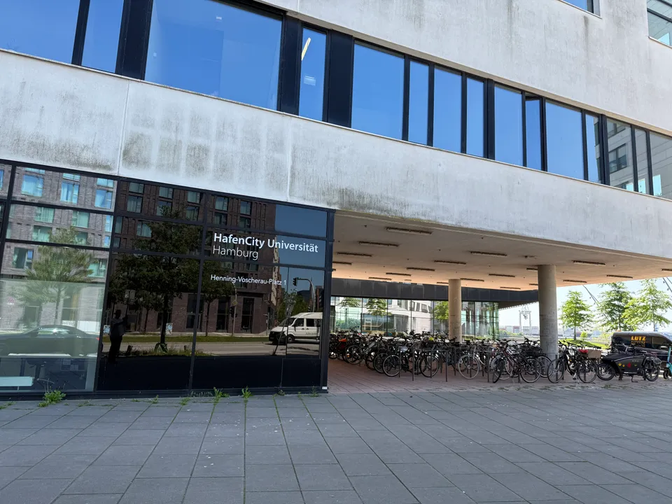 Gebäudeecke mit Schriftzug HafenCity Universität Hamburg und überdachtem Fahrradabstellplatz unter auskragendem Obergeschoss