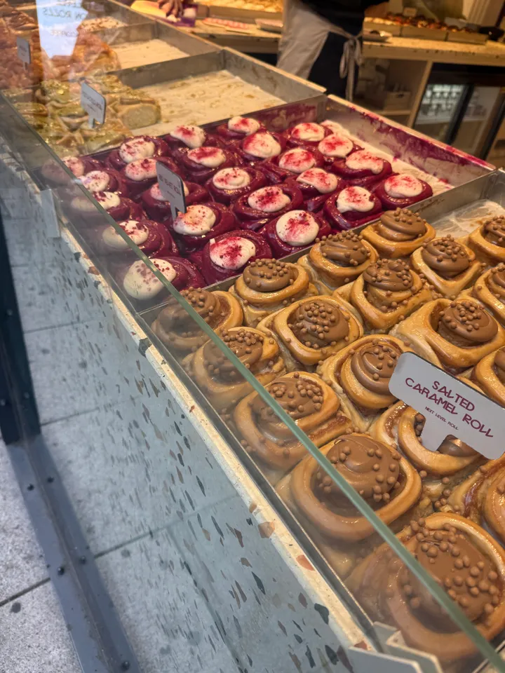 Verkaufstheke mit Zimtschnecken, vorne Salted Caramel Rolls mit Knusperperlen, dahinter rote Schnecken mit weißem Topping