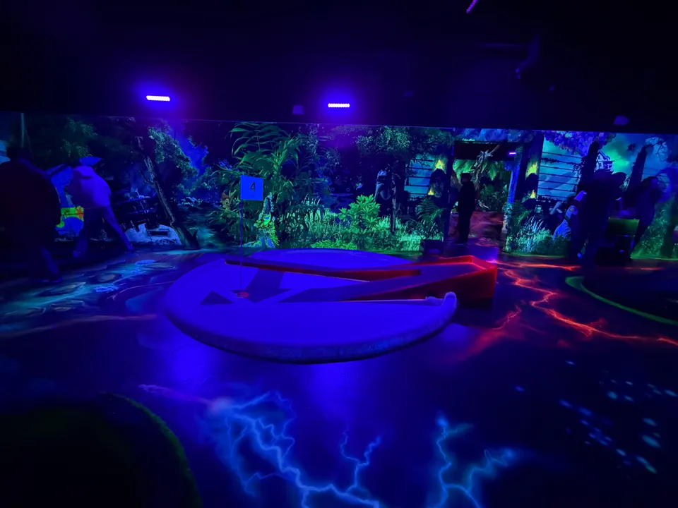 Minigolfbahn Nummer 4 im Schwarzlicht vor Dschungelkulisse, Boden mit leuchtendem Blitzmuster