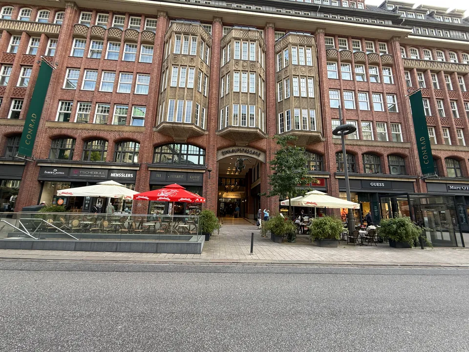 Backsteinfassade des Levantehauses mit drei Natursteinerkern, Passageneingang, Ladengeschäften und Außengastronomie mit Sonnenschirmen an der Mönckebergstraße