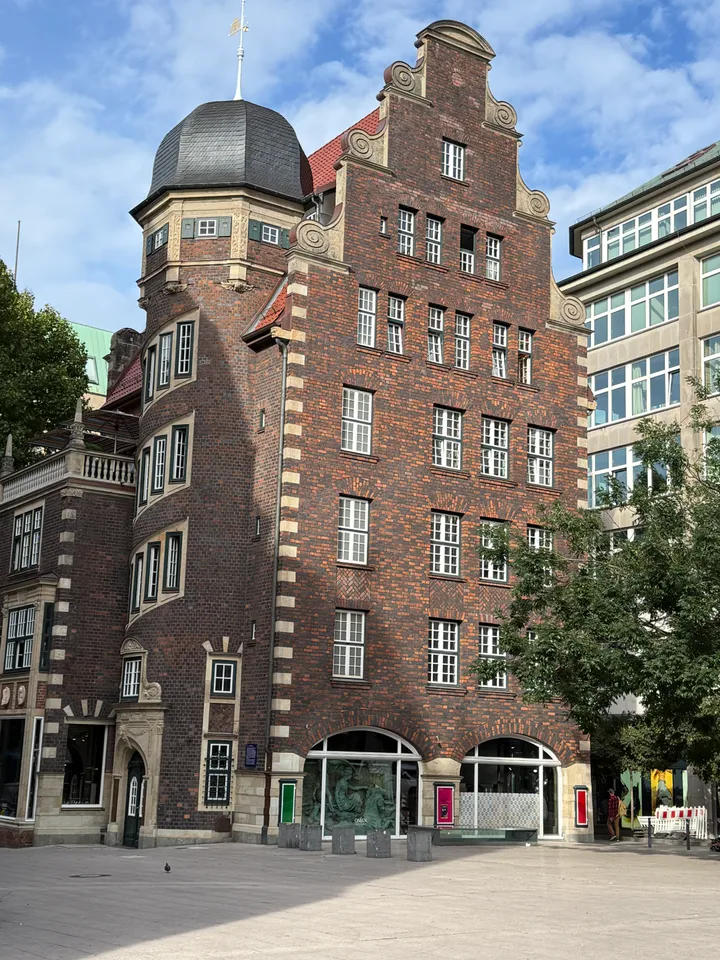 Backsteinfassade mit geschweiftem Treppengiebel, Rundturm mit Schieferhaube und zwei Rundbogenfenstern im Erdgeschoss