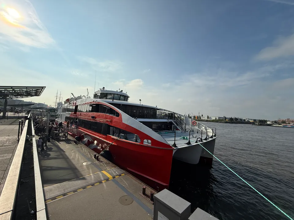 Bug eines rot-weißen Katamarans am Ponton an der Elbe, am Anleger eine wartende Menschenschlange