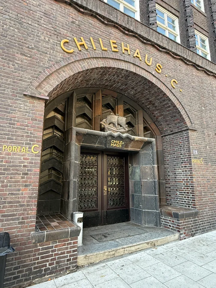 Rundbogenportal C des Chilehauses mit goldenem Schriftzug, Schiffsrelief und verzierter dunkler Doppeltür