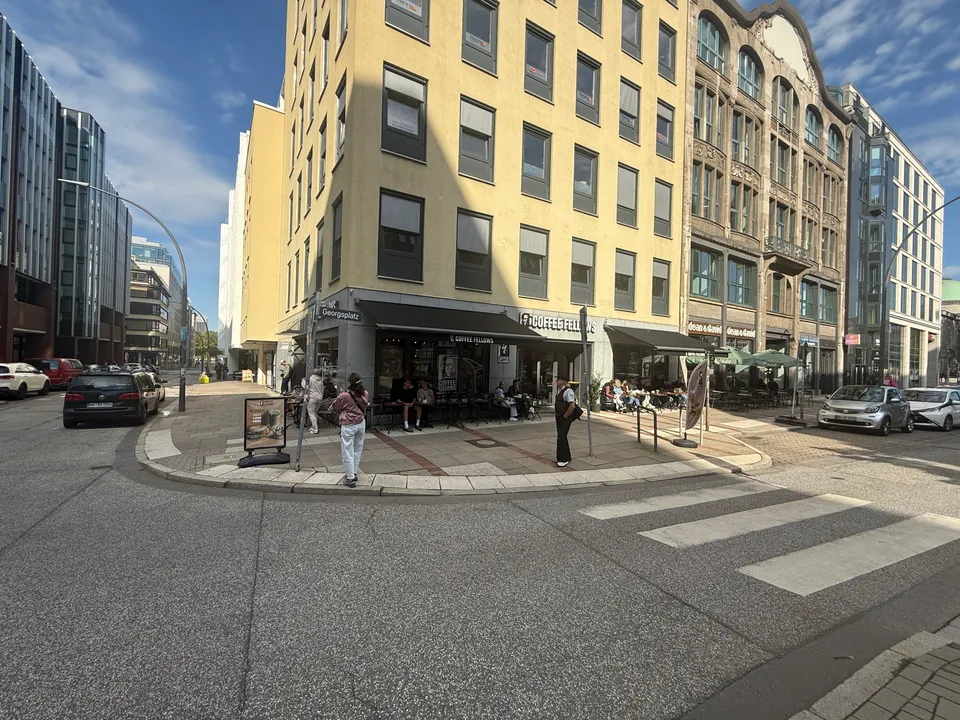 Eckgebäude am Georgsplatz mit Café Coffee Fellows, Markisen, Außenterrasse und Zebrastreifen bei Sonnenschein
