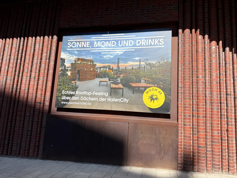 Werbeplakat für die Rooftop-Bar Moon 46 mit Dachterrassenmotiv an einer gewellten Klinkerfassade
