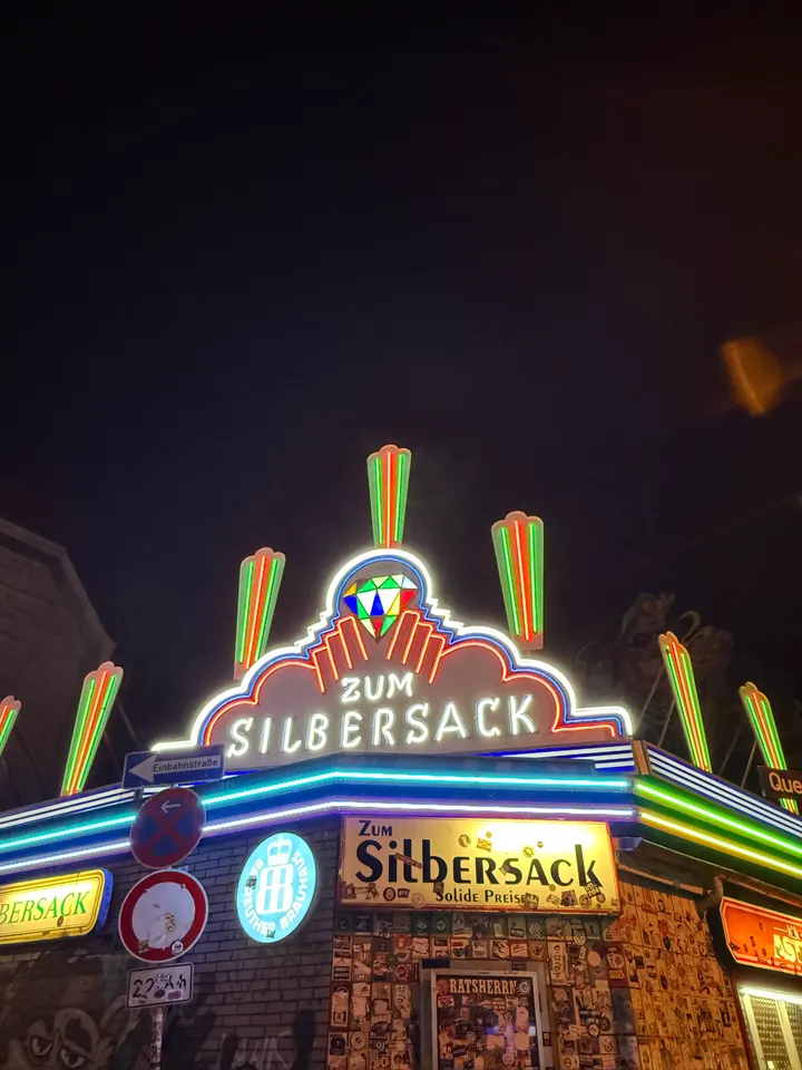 Neon-Leuchtreklame „Zum Silbersack“ mit buntem Diamant-Emblem vor dunklem Nachthimmel