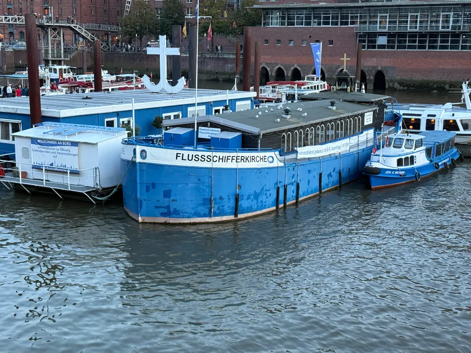 Blaues Kirchenschiff mit Schriftzug Flussschifferkirche, daneben ein Anlegeponton und ein kleines Boot im Hamburger Binnenhafen