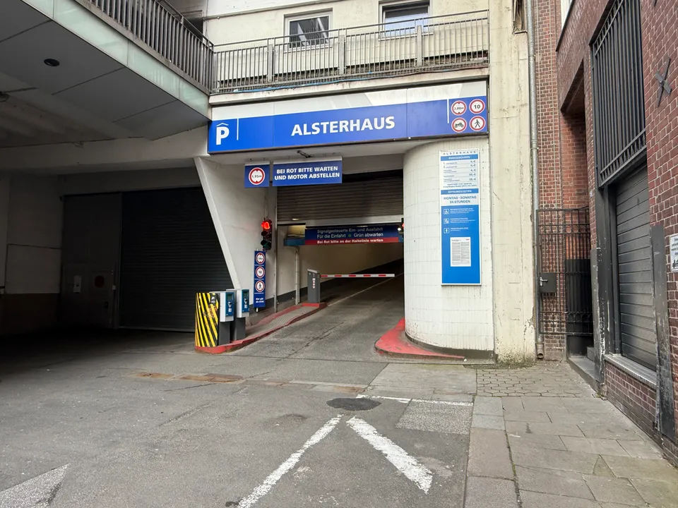 Einfahrt des Parkhauses Alsterhaus mit blauem Schild, Schranke, Ticketautomaten, roter Ampel und abwärts führender Rampe