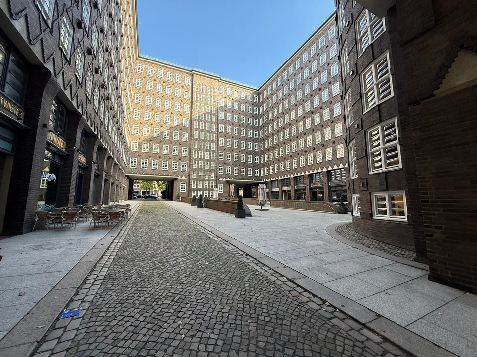 Innenhof des Sprinkenhofs mit hohen Klinkerfassaden, gepflasterter Gasse, Durchfahrt und leerer Außenbestuhlung