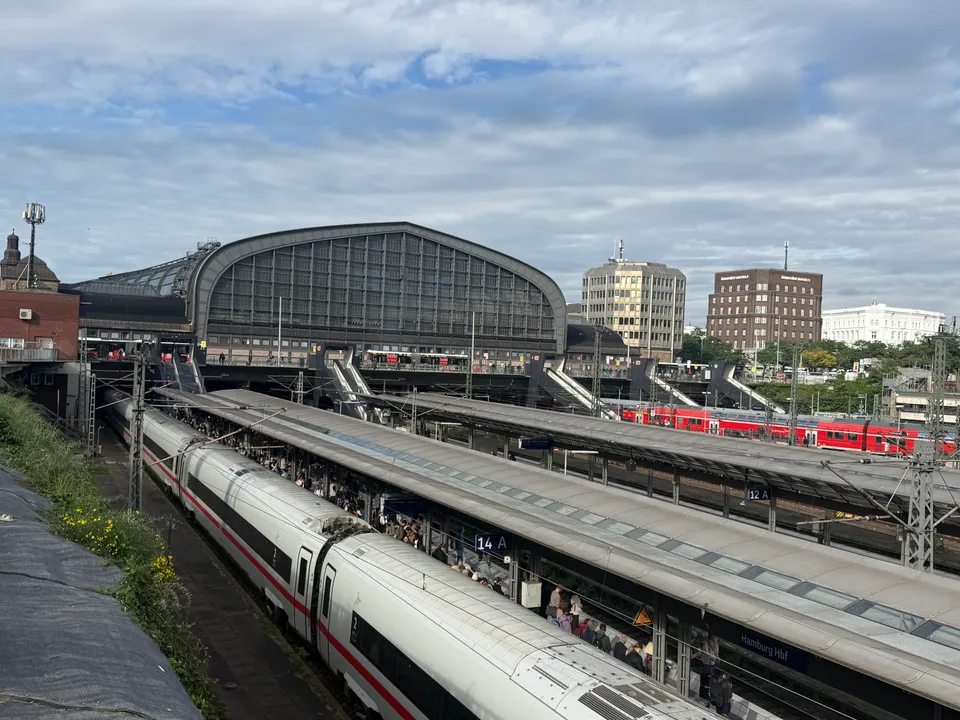 ICE und roter Regionalzug an überdachten Bahnsteigen vor der gewölbten Halle des Hamburger Hauptbahnhofs