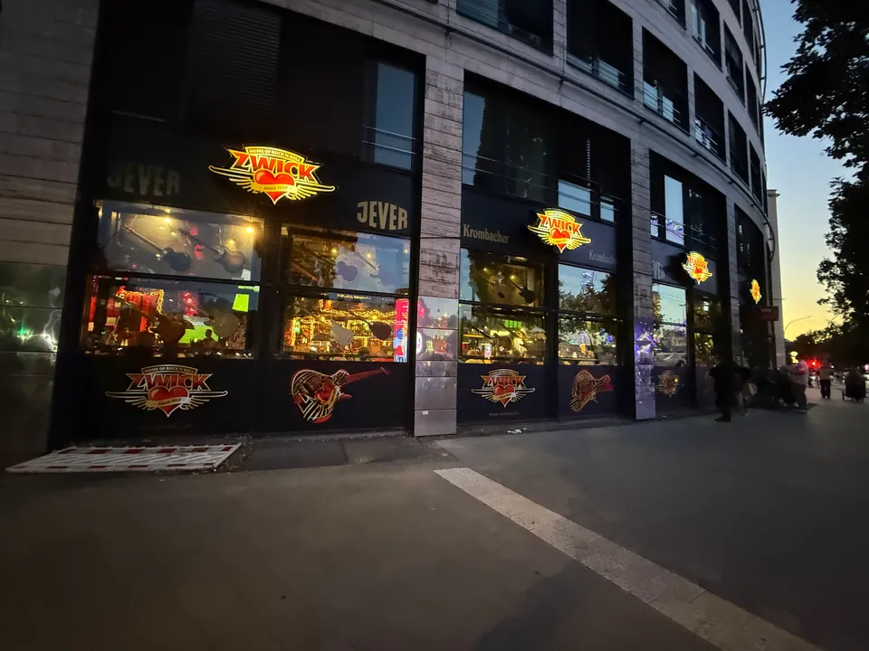 Beleuchtete Fassade der Rockkneipe ZWICK mit Leuchtlogos, Bierwerbung und Schaufenstern in der Abenddämmerung