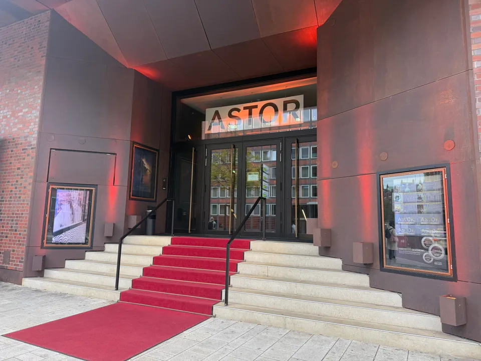 Eingang des ASTOR-Kinos mit Steintreppe, rotem Teppich, Glastüren und rot beleuchteter Metallfassade