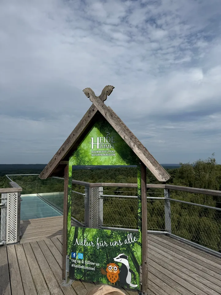 Fotowand mit Holzgiebel und Heide-Himmel-Logo auf einer Aussichtsplattform, dahinter weite Waldlandschaft
