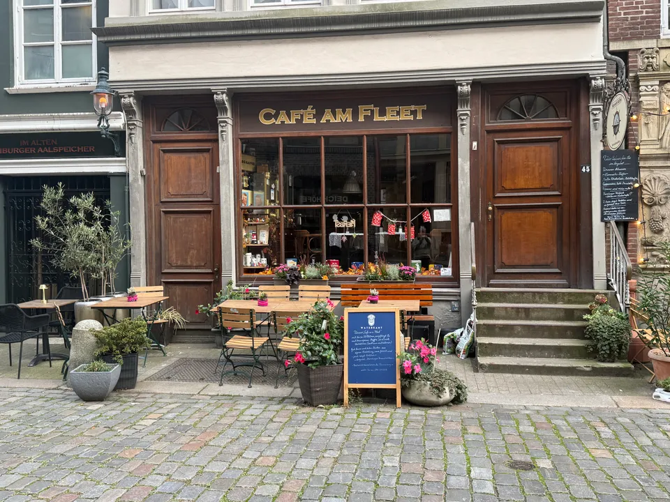 Historische Holzfassade des Café am Fleet mit Schaufenster, Außentischen und Blumenkübeln auf Kopfsteinpflaster