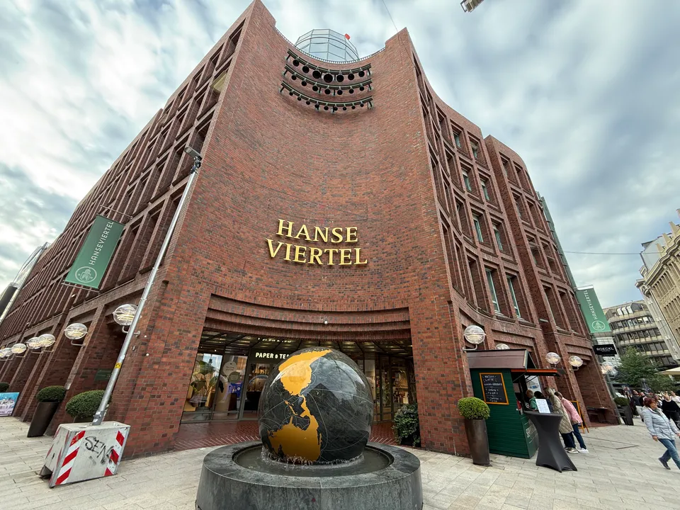Geschwungene Backsteinecke mit goldenem Schriftzug Hanse Viertel und Globusbrunnen vor dem Eingang